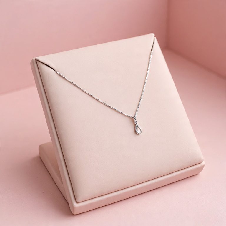 Silver teardrop pendant necklace on a pink jewelry display.